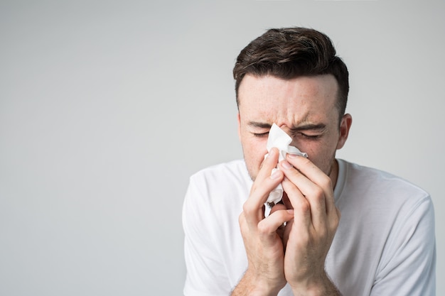 Photo young man isolated over background portrait of guy sneezing into white napkin