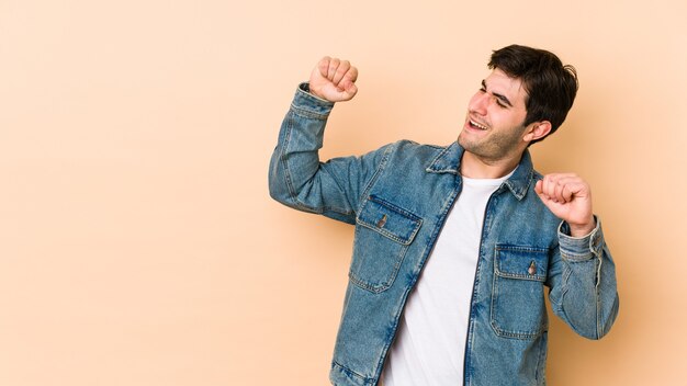 Young man isolated on beige celebrating a special day, jumps and raise arms with energy.