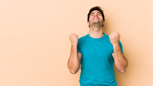 Young man isolated on beige space celebrating a victory, passion and enthusiasm, happy expression.