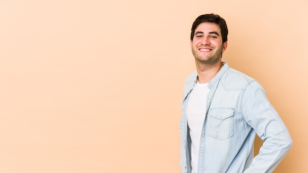 Young man isolated on beige space confident keeping hands on hips.