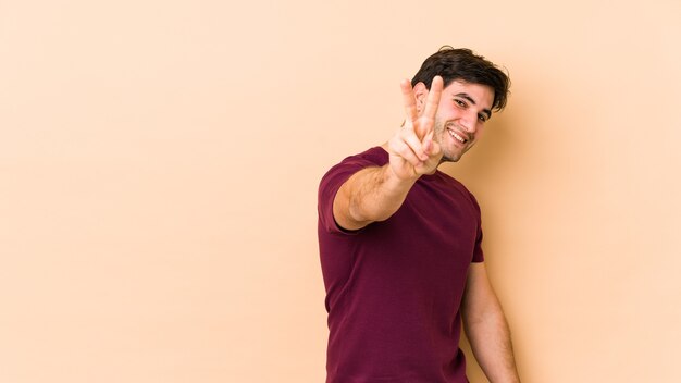 Young man isolated on beige wall joyful and carefree showing a peace symbol with fingers.