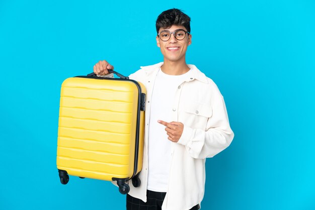 Young man on isolated blue in vacation with travel suitcase