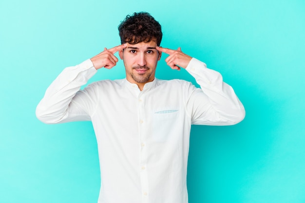 Young man isolated on blue wall focused on a task, keeping forefingers pointing head