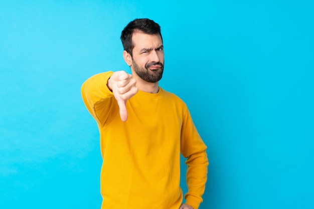 Young man over isolated blue wall showing thumb down with negative expression