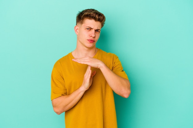 Young man isolated on blue wall showing a timeout gesture