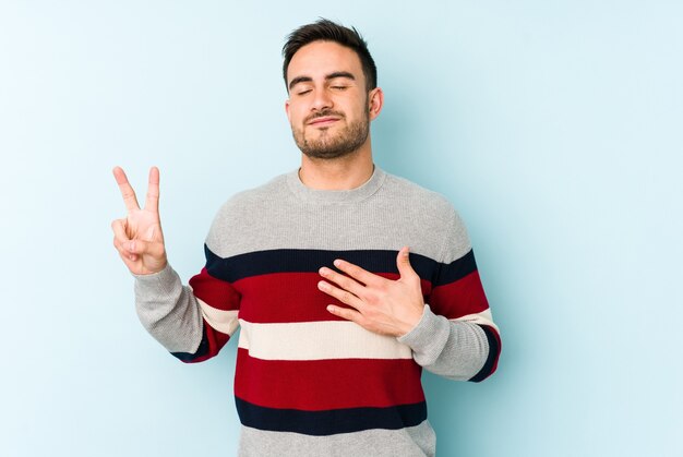 Young man isolated on blue wall taking an oath, putting hand on chest