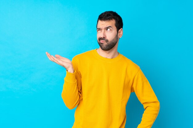 Young man over isolated blue wall unhappy for not understand something