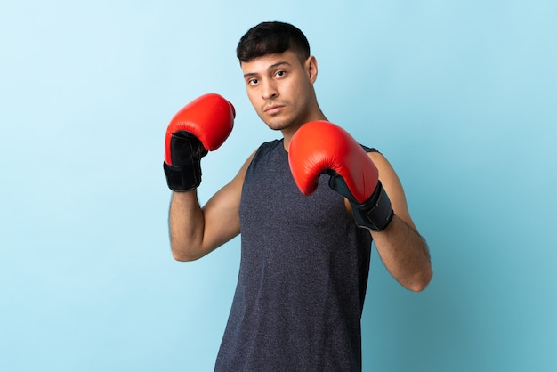 Young man isolated on blue with boxing gloves