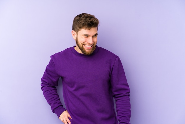 Фото Молодой человек, изолированный на фиолетовой стене, смеется и закрывает глаза, чувствует себя расслабленным и счастливым