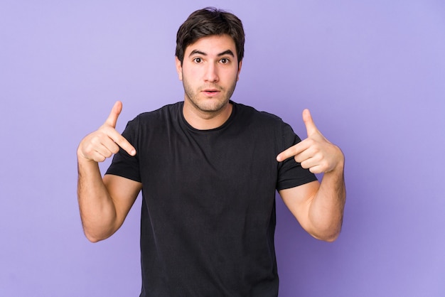 Young man isolated on purple background points down with fingers, positive feeling.