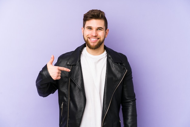 Young man isolated on purple person pointing by hand to a shirt copy space, proud and confident