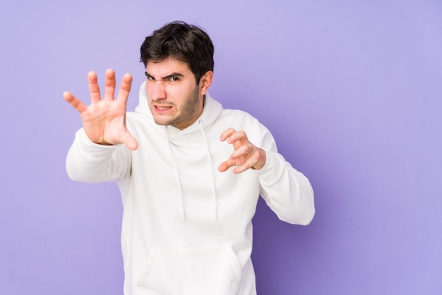 Young man isolated on purple showing claws imitating a cat, aggressive gesture.