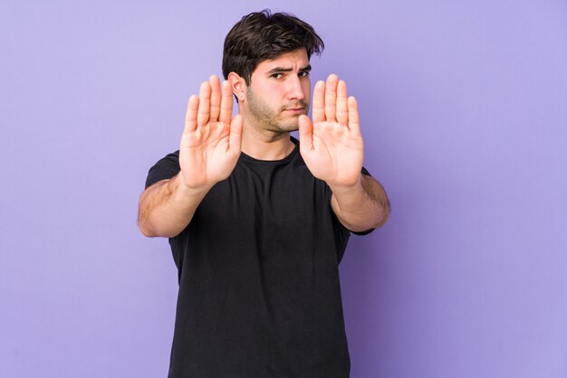 Young man isolated on purple standing with outstretched hand showing stop sign, prevonting you.