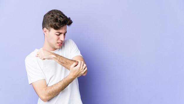 Young man isolated on purple wall massaging elbow, suffering after a bad movement