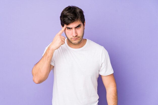 Young man isolated on purple wall pointing temple with finger, thinking, focused on a task.