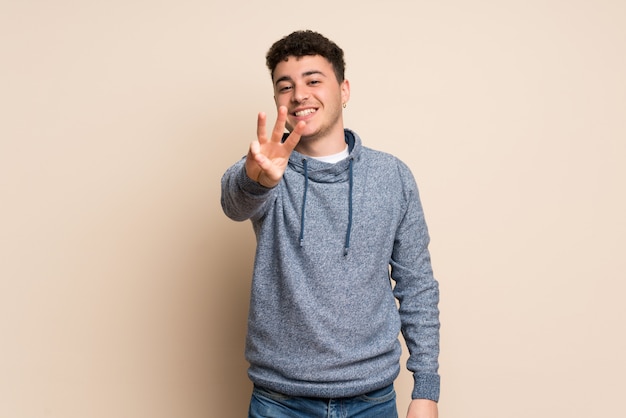 Young man over isolated wall happy and counting three with fingers