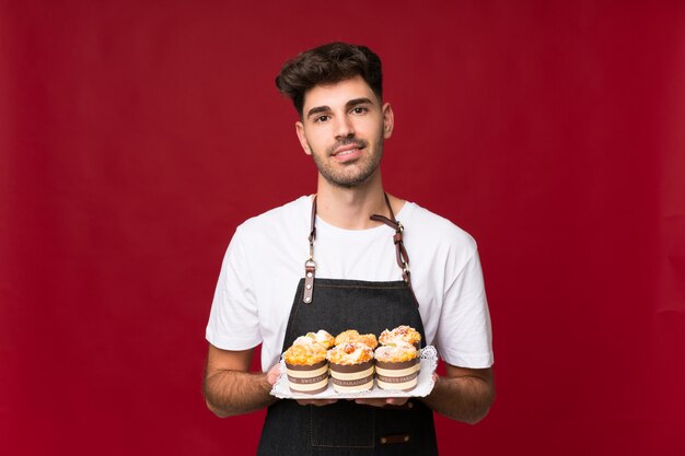 Young man over isolated wall holding mini cakes