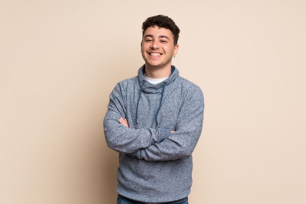 Young man over isolated wall keeping the arms crossed in frontal position