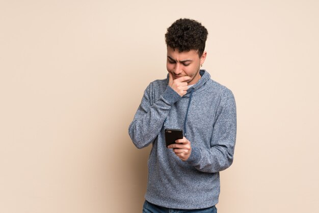 Young man over isolated wall thinking and sending a message