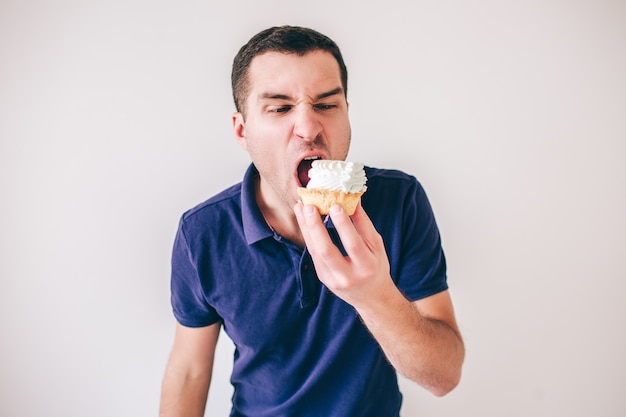 Young man isolated over white background. Guy stand alone and bite piece of small cake. Dessert and delicious time. Yummy food.