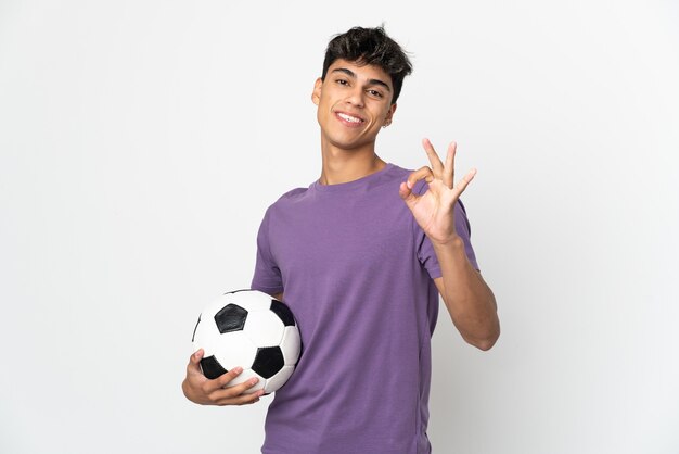 Young man over isolated white background with soccer ball and making OK sign