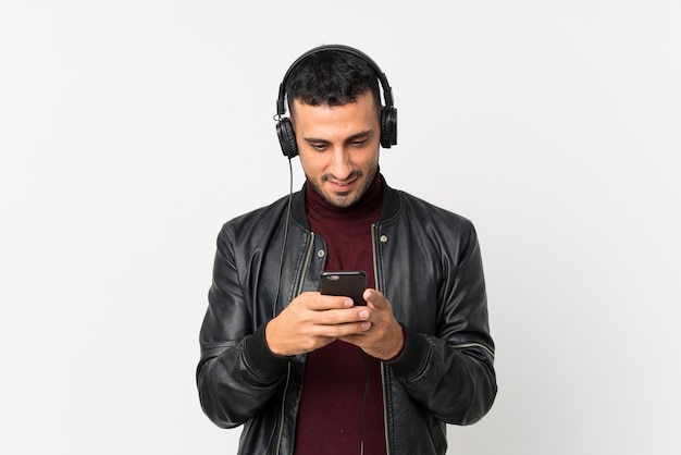 Young man over isolated white using the mobile with headphones