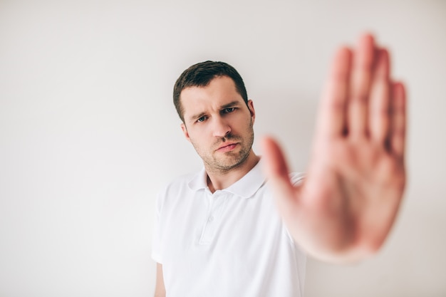 Young man isolated over white wall. Guy show stop symbol with hand. Picture of blurred human palm.