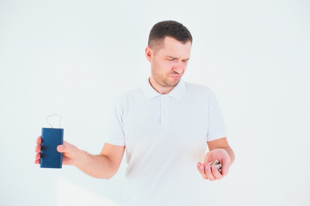 Young man isolated over white wall. Unhappy guy holding batteries and power bank in hands and looking at them. Recycling time for no waste lifestyle.