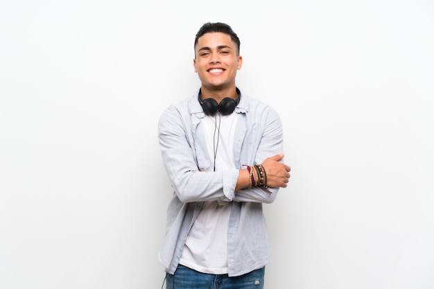 Young man over isolated white wall with earphones smiling a lot