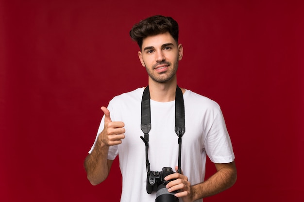 Молодой человек над изолированной с профессиональной камерой и с большим пальцем вверх