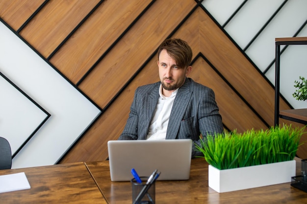 A young man in a jacket is sitting in the office at a laptop