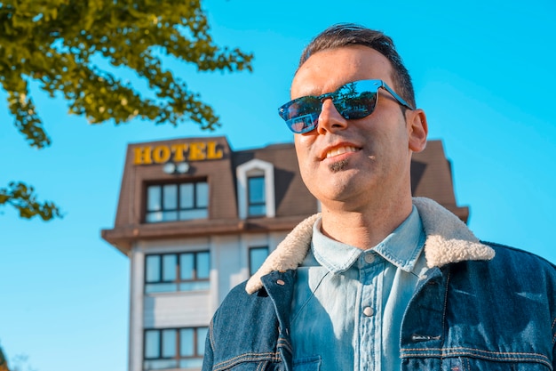 young man in a jacket and sunglasses next to the hotel