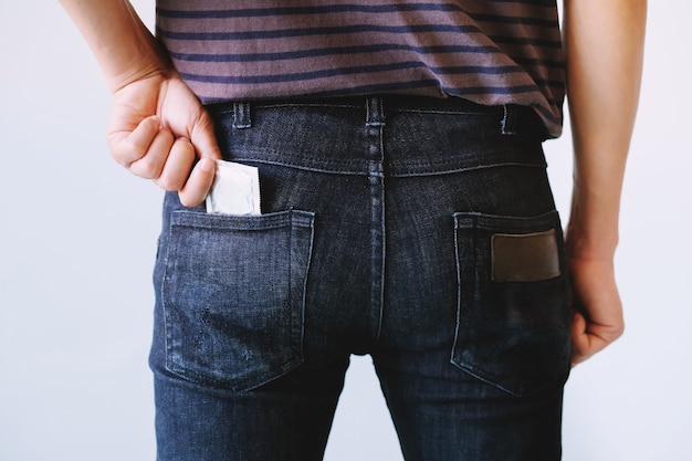 Foto tasca laterale posteriore dei jeans del giovane per trasportare i preservativi tenendo in mano il preservativo dai jeans.