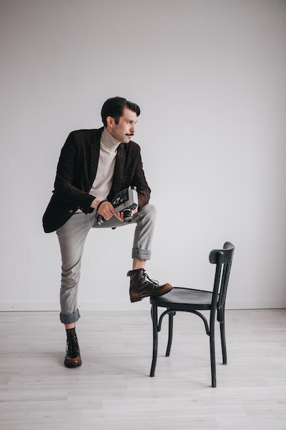 A young man in jeans and a jacket poses against a white wall in the studio