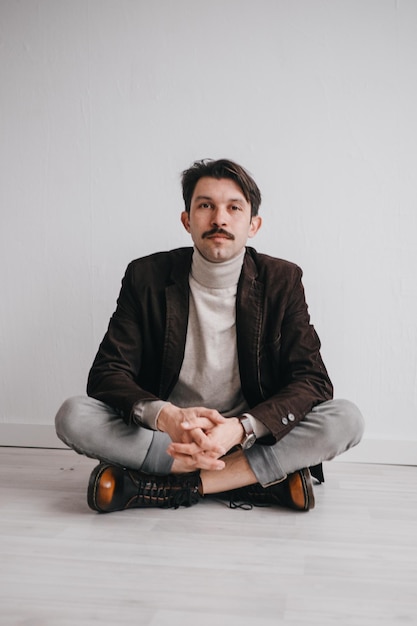 Foto un giovane in jeans e giacca posa contro un muro bianco in studio