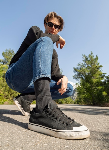 Young man in jeans and sneakers sits on the road in the woods