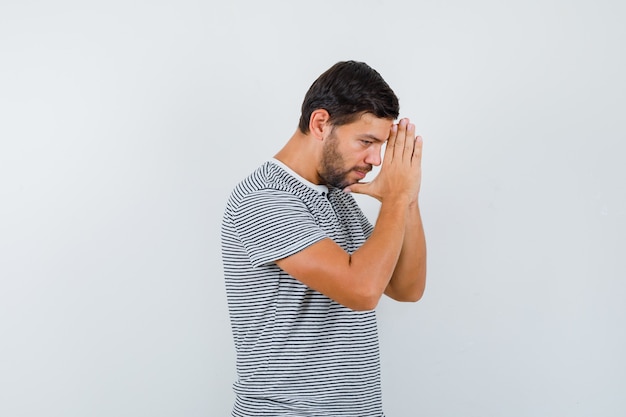 Young man keeping hands in praying gesture in t-shirt and looking hopeful. front view.