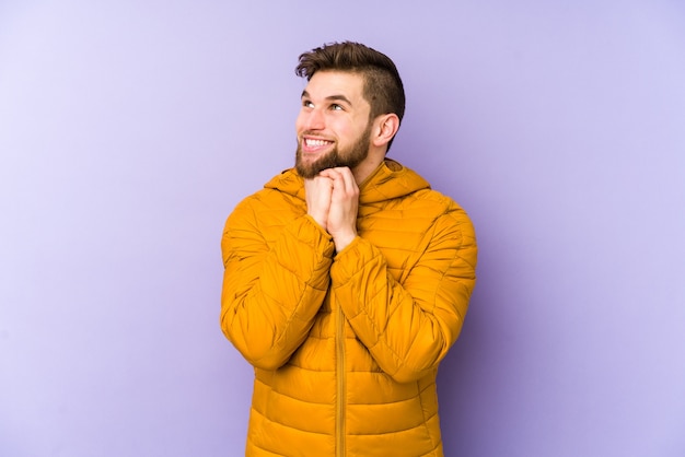 Young man keeps hands under chin, is looking happily aside.