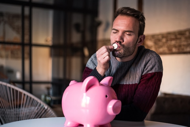 Young man kissing a coin with a piggy bank