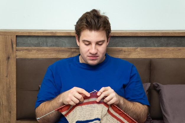 Young man knitting a striped sweater at home New hobby knitting The knitting project is underway