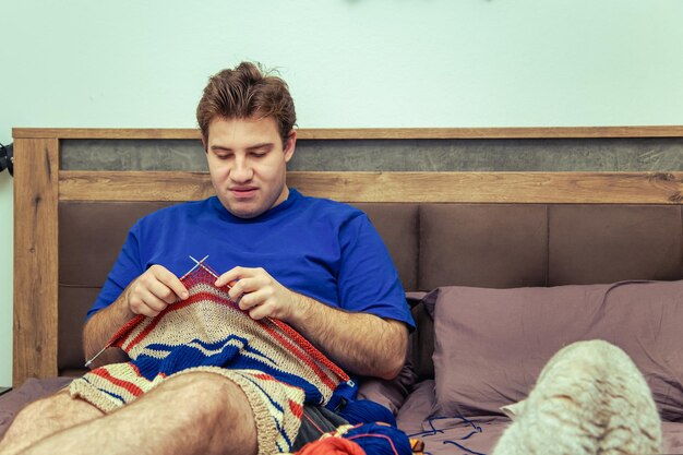 Young man knitting a striped sweater at home