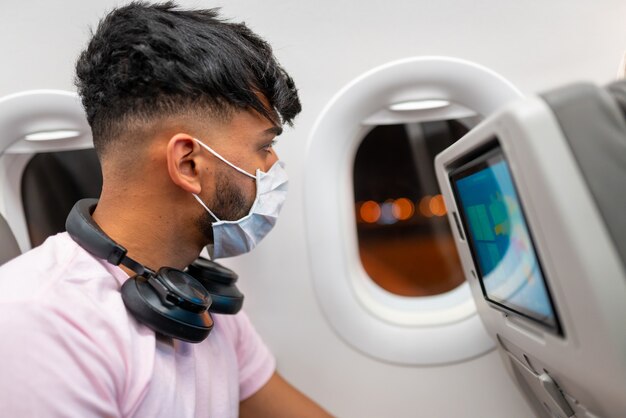 Young man latin american wearing protective face mask, traveling by plane