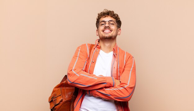 Young man laughing happily with arms crossed, with a relaxed, positive and satisfied pose