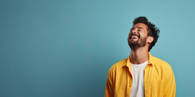 Young man laughing joyful in yellow tshirt Isolated on blue background studio portrait