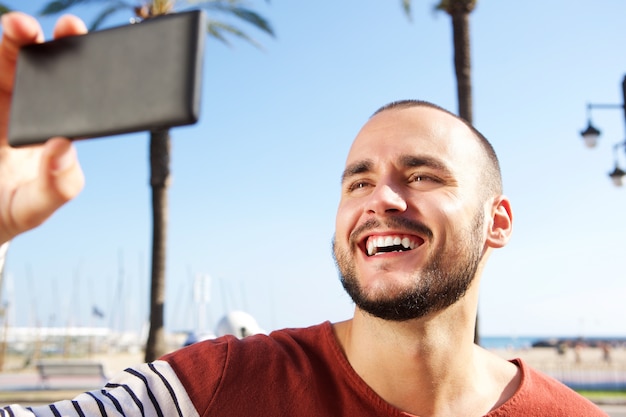 Photo young man laughing when taking a selfie with mobile phone