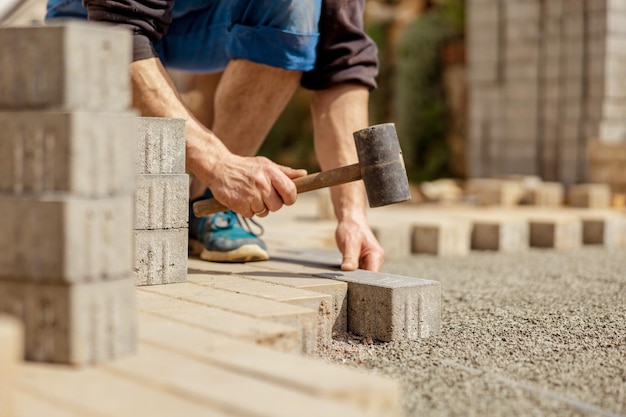 Young man laying gray concrete paving slabs in house courtyard on gravel foundation base Master lays paving stones Garden brick pathway paving by professional paver worker Repairing sidewalk