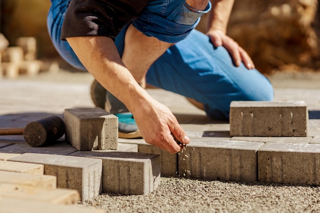 Young man laying gray concrete paving slabs in house courtyard on gravel foundation base Master lays paving stones Garden brick pathway paving by professional paver worker Repairing sidewalk