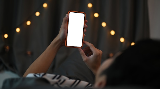 Молодой человек, лежа на кровати и используя смартфон ночью.