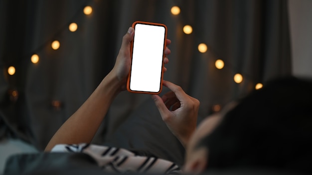 Young man laying on his bed and using smart phone at night.