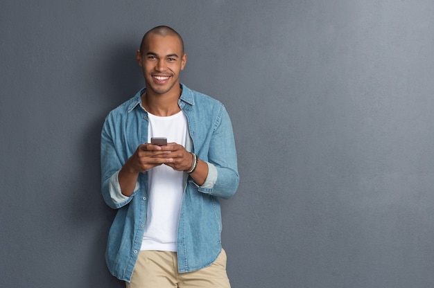 Young man leaning against a grey wall using mobile phone